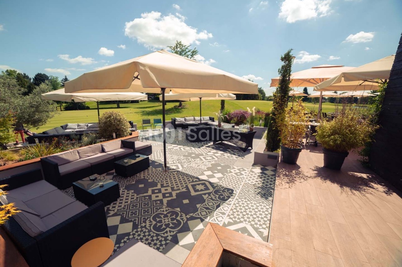 Terrasse aménagée avec salons de jardin, parasols et vue sur un espace vert parsemé d'arbres sous un ciel dégagé.