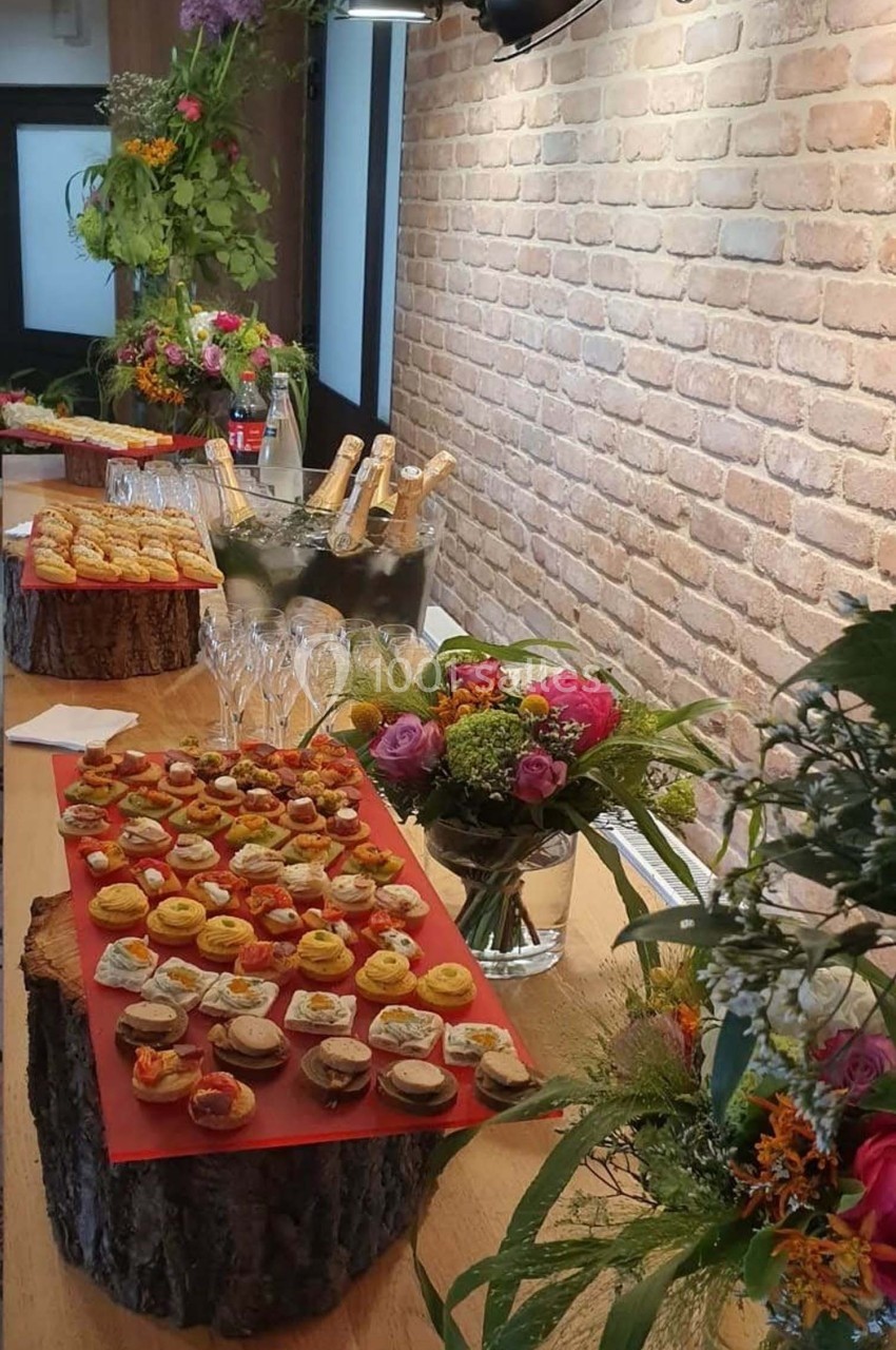 Plateau de bouchées apéritives variées disposé sur une table en bois, décorée de fleurs et de bouteilles.