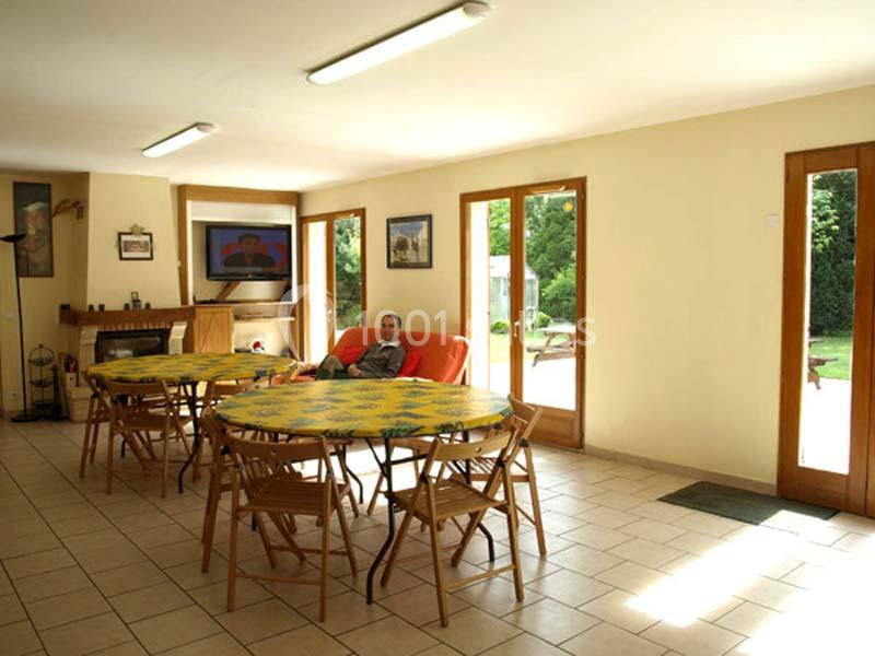 Salle à manger lumineuse avec plusieurs tables rondes, un homme assis sur un canapé et des portes vitrées donnant sur un…