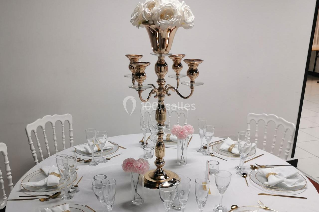 Table élégamment dressée avec un chandelier doré, des roses blanches et roses, et une vaisselle raffinée.