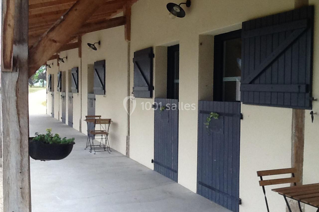 Façade d'un bâtiment avec des volets bleus, des tables en bois et un toit en bois sous une galerie couverte.