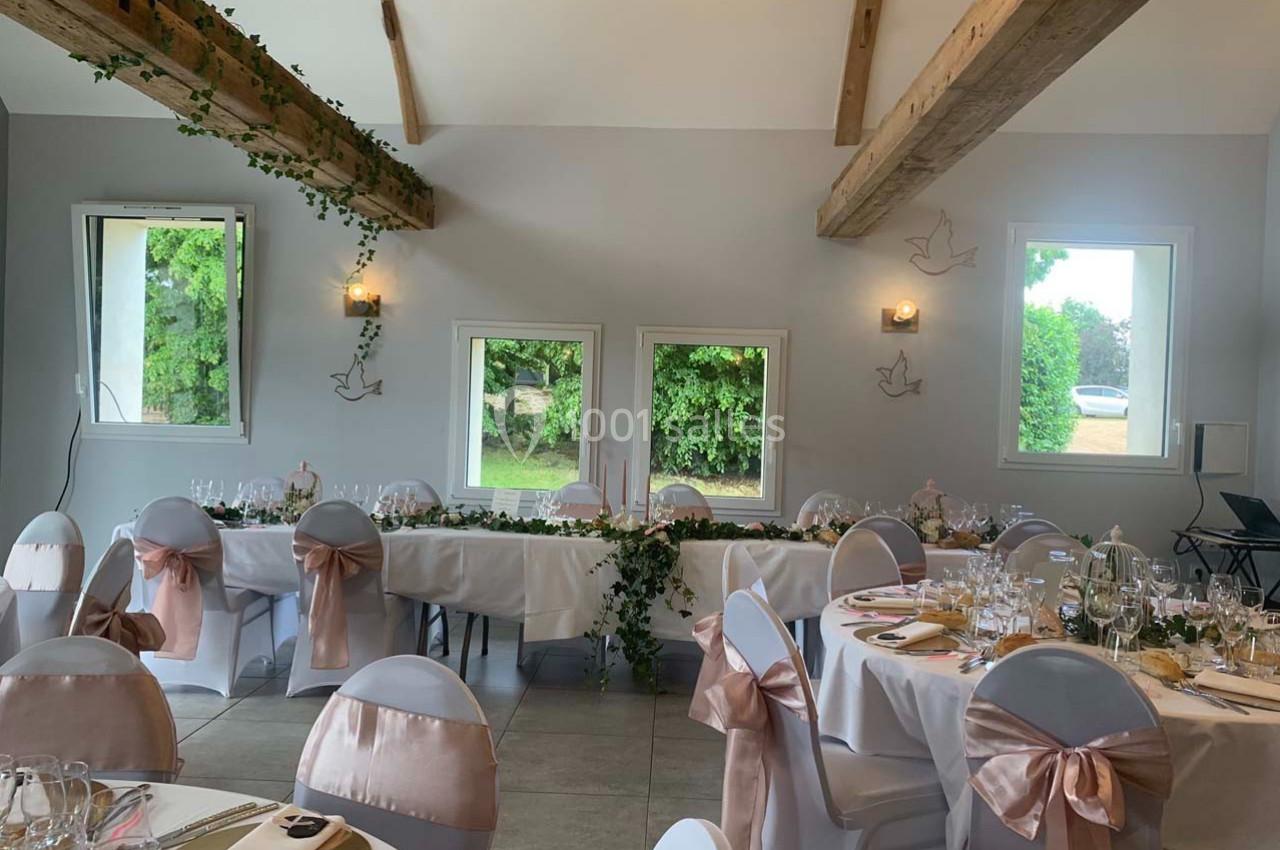 Salle de réception décorée avec des nappes blanches, chaises ornées de nœuds roses et guirlandes de feuillage.