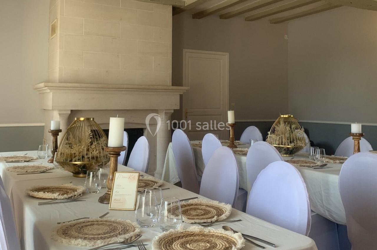 Salle de réception avec tables dressées, nappes blanches, assiettes en fibres naturelles et bougeoirs décoratifs.