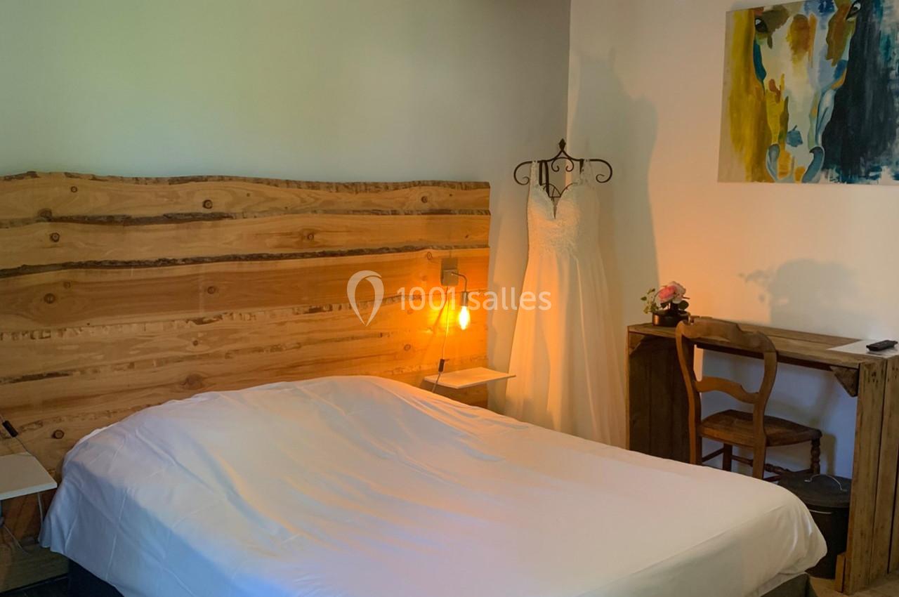 Chambre avec lit double, tête de lit en bois, bureau, chaise, robe blanche sur un mannequin et tableau coloré au mur.