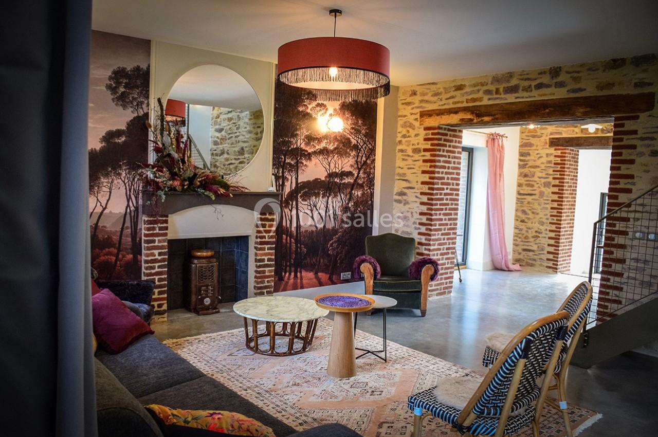 Salon chaleureux avec murs en pierre et briques, cheminée décorée, mobilier éclectique et grande ouverture lumineuse.