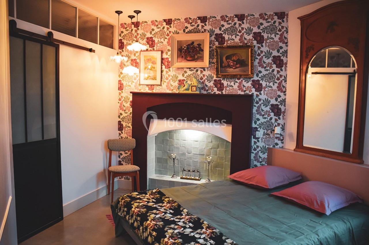 Chambre avec lit double, cheminée décorative, miroir, chaises et mur tapissé de motifs floraux.