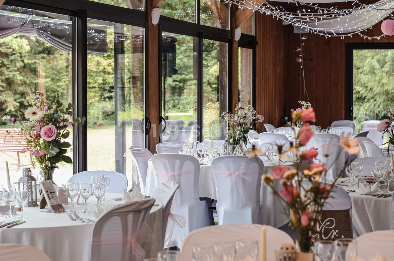Salle de réception décorée pour un mariage, avec des tables dressées, nappes blanches et fleurs colorées.
