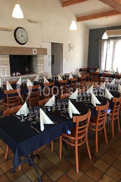 Salle de restaurant avec tables dressées, nappes noires, serviettes pliées en pointe et chaises en bois.