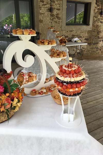 Plateau de buffet avec brochettes apéritives, pains garnis et décorations florales sur une table en extérieur.