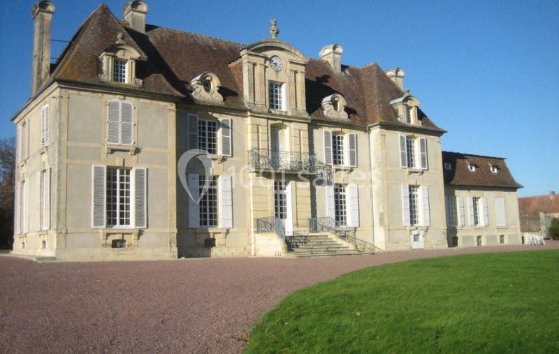 Location salle Brouay (Calvados) - Château de Brouay #6 Façade d'un château ancien en pierre avec toit en tuiles, volets blancs et pelouse au premier plan.