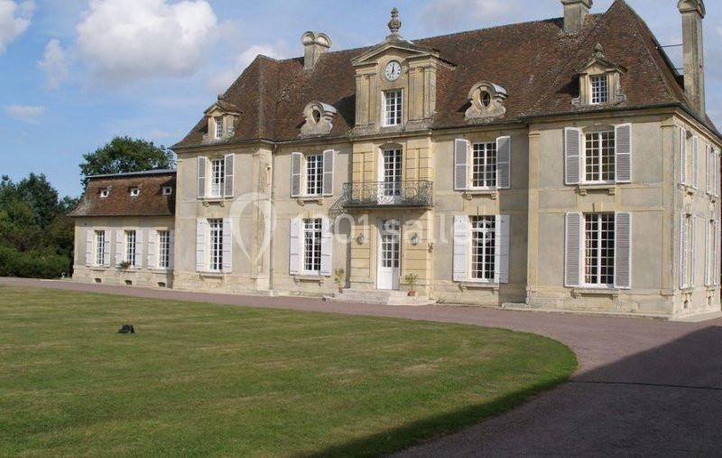 Location salle Brouay (Calvados) - Château de Brouay #11 Façade d'un manoir ancien en pierre avec toit en ardoise, entouré d'une pelouse et d'un ciel partiellement nuageux.