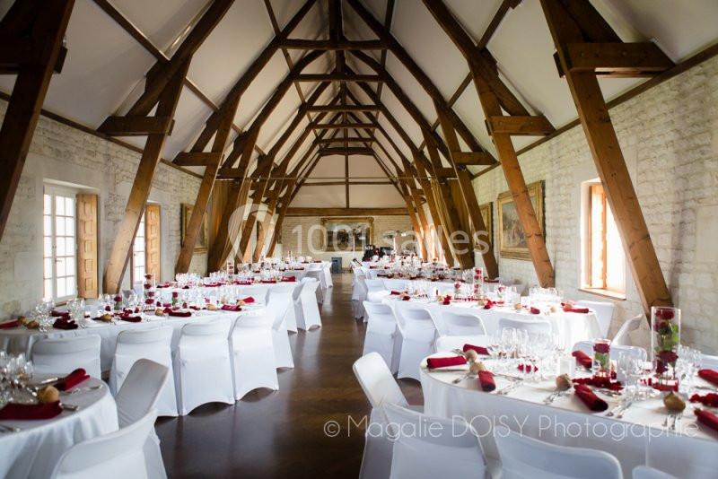 Location salle Brouay (Calvados) - Château de Brouay #3 Salle de réception lumineuse avec des tables rondes dressées, nappes blanches et décorations rouges, poutres apparentes.
