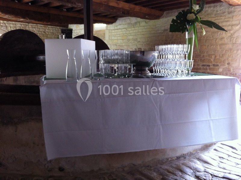 Location salle Brouay (Calvados) - Château de Brouay #12 Table dressée avec une nappe blanche, contenant des verres, carafes et une coupe, dans un cadre en pierre rustique.