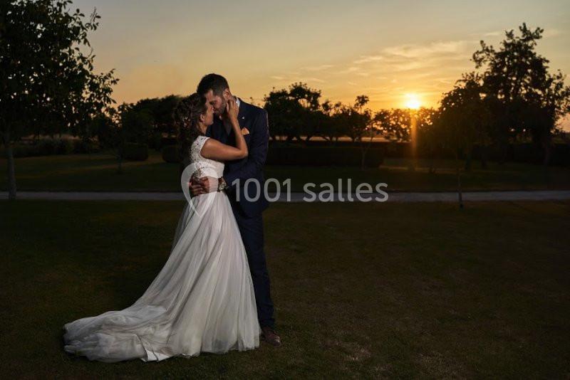 Un couple en tenue de mariage s'embrasse dans un parc au coucher du soleil.