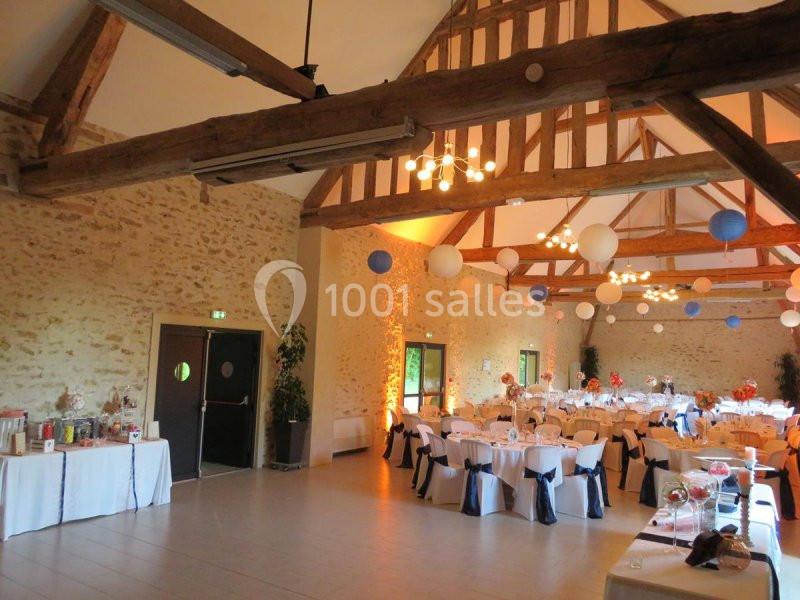 Salle de réception avec murs en pierre, poutres apparentes et tables rondes décorées pour un événement festif.