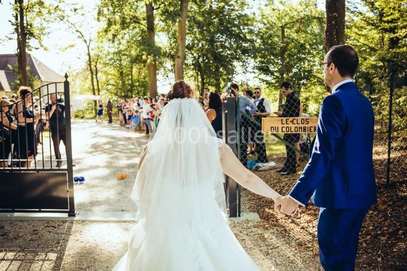 Un couple de mariés entre dans une cour extérieure, main dans la main, sous le regard des invités.