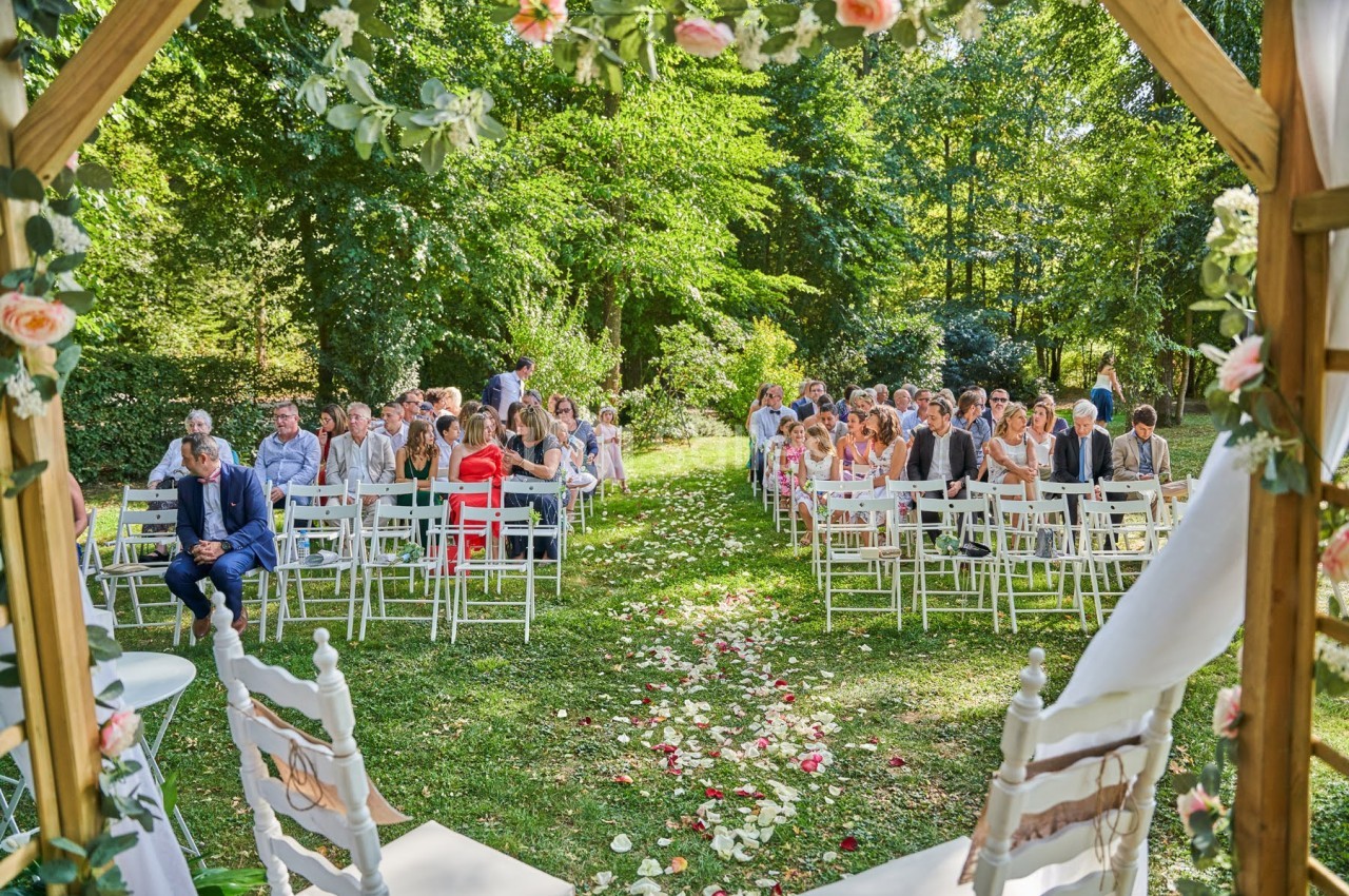 Cérémonie de mariage en plein air avec des invités assis sur des chaises blanches, entourés de verdure et de décorations…