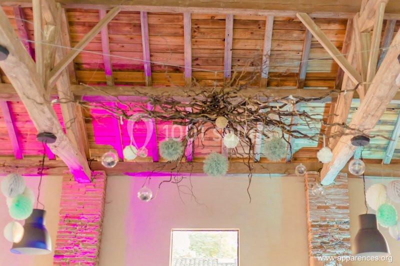 Décoration suspendue avec branches et boules lumineuses dans une salle au plafond en bois et briques apparentes.