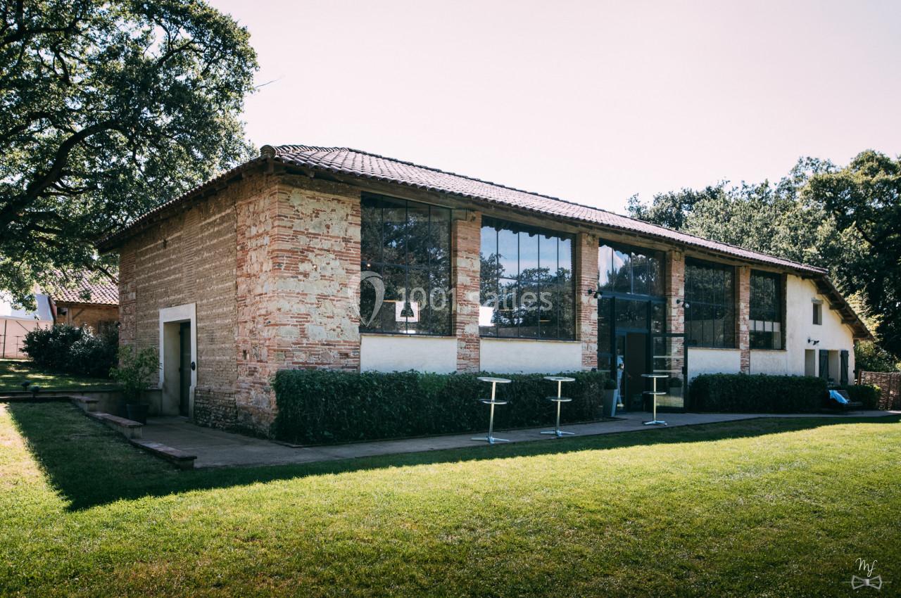 Bâtiment en briques avec de grandes fenêtres, entouré de verdure et éclairé par une lumière naturelle.
