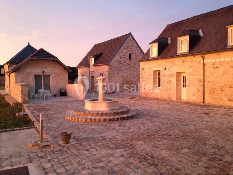 Cour pavée avec une fontaine centrale entourée de bâtiments en pierre sous un éclairage de coucher de soleil.