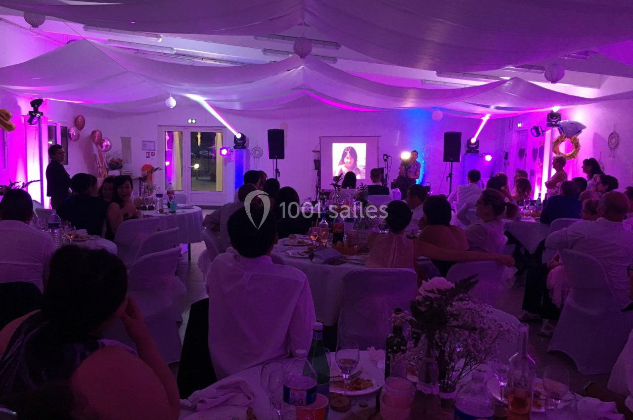 Salle décorée pour une réception, avec des invités assis à des tables et une projection d'image sur un écran.