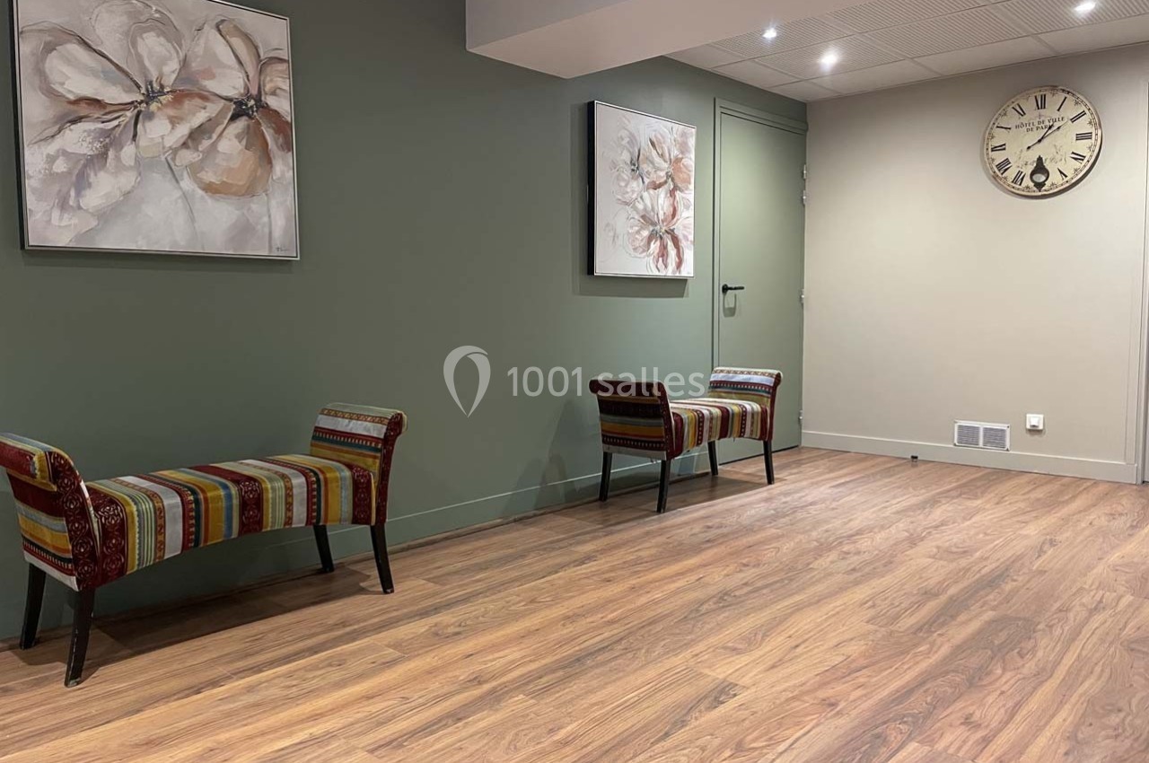 Salle d'attente avec bancs colorés, tableaux floraux sur un mur vert et une horloge murale beige.