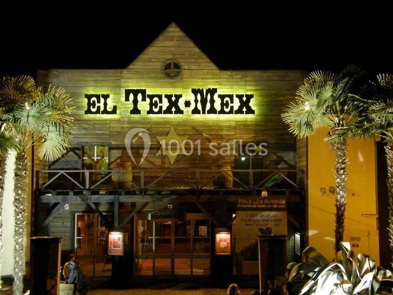 Façade en bois d'un restaurant nommé ’El Tex-Mex’ éclairée la nuit, entourée de palmiers.