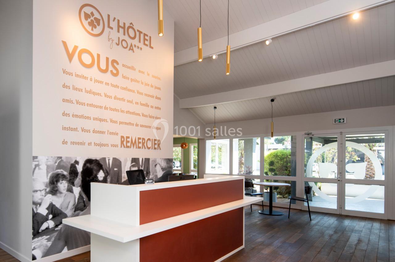 Accueil d'un hôtel avec un comptoir moderne, des luminaires suspendus et une grande baie vitrée donnant sur l'extérieur.