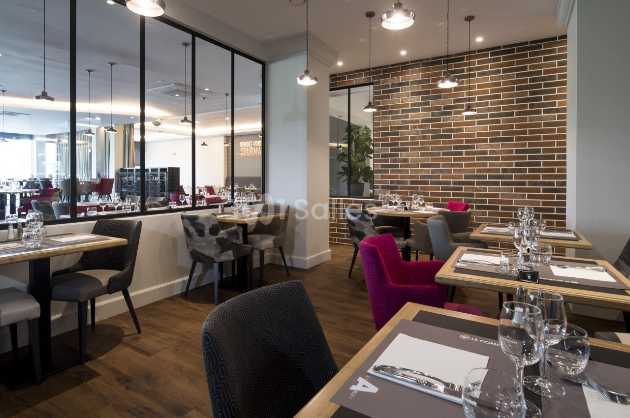 Salle de restaurant moderne avec tables dressées, chaises variées et murs en briques apparentes.