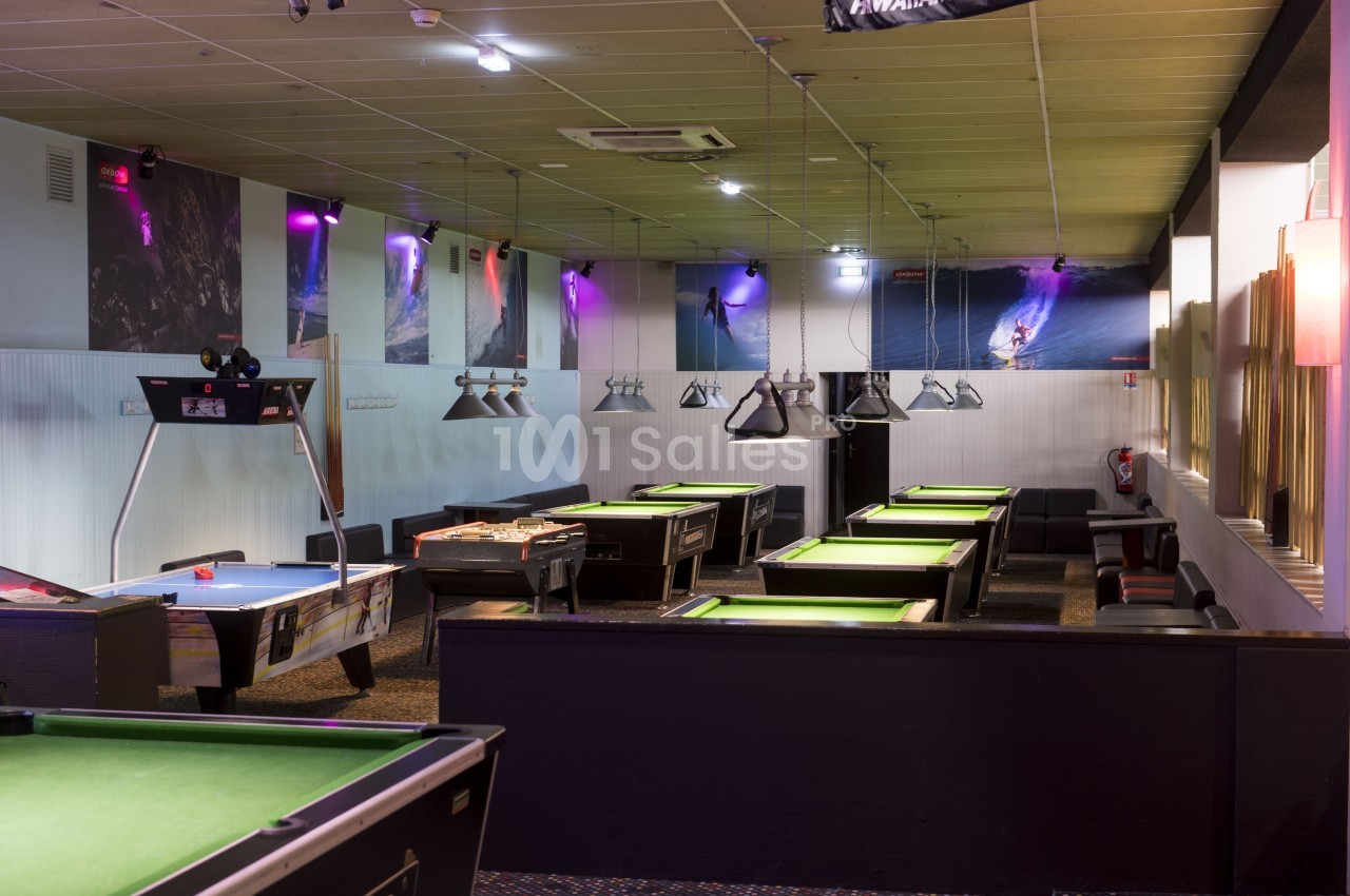 Salle de jeux intérieure avec tables de billard, baby-foot et éclairage tamisé.