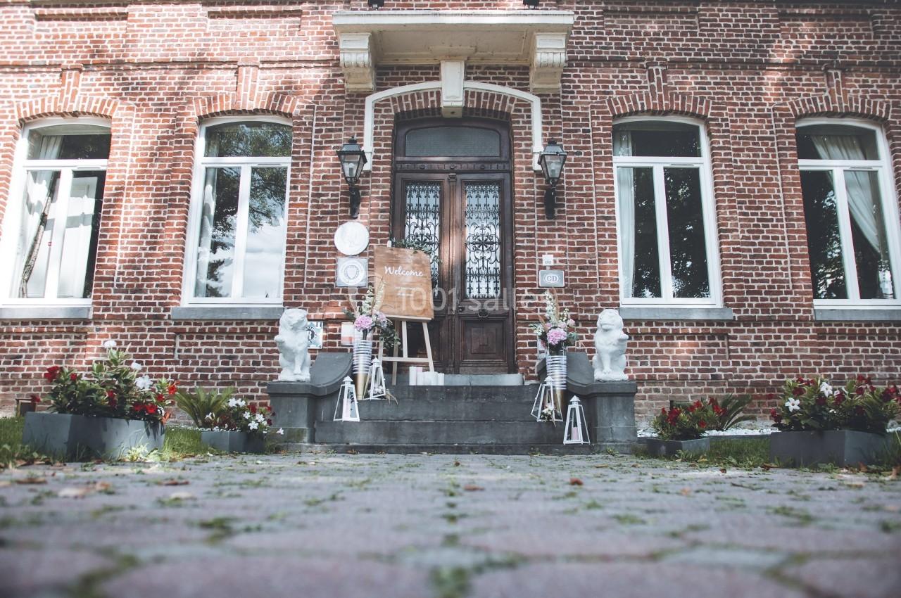 Façade en briques rouges d'une maison avec une porte centrale, décorée de fleurs et de statues blanches.