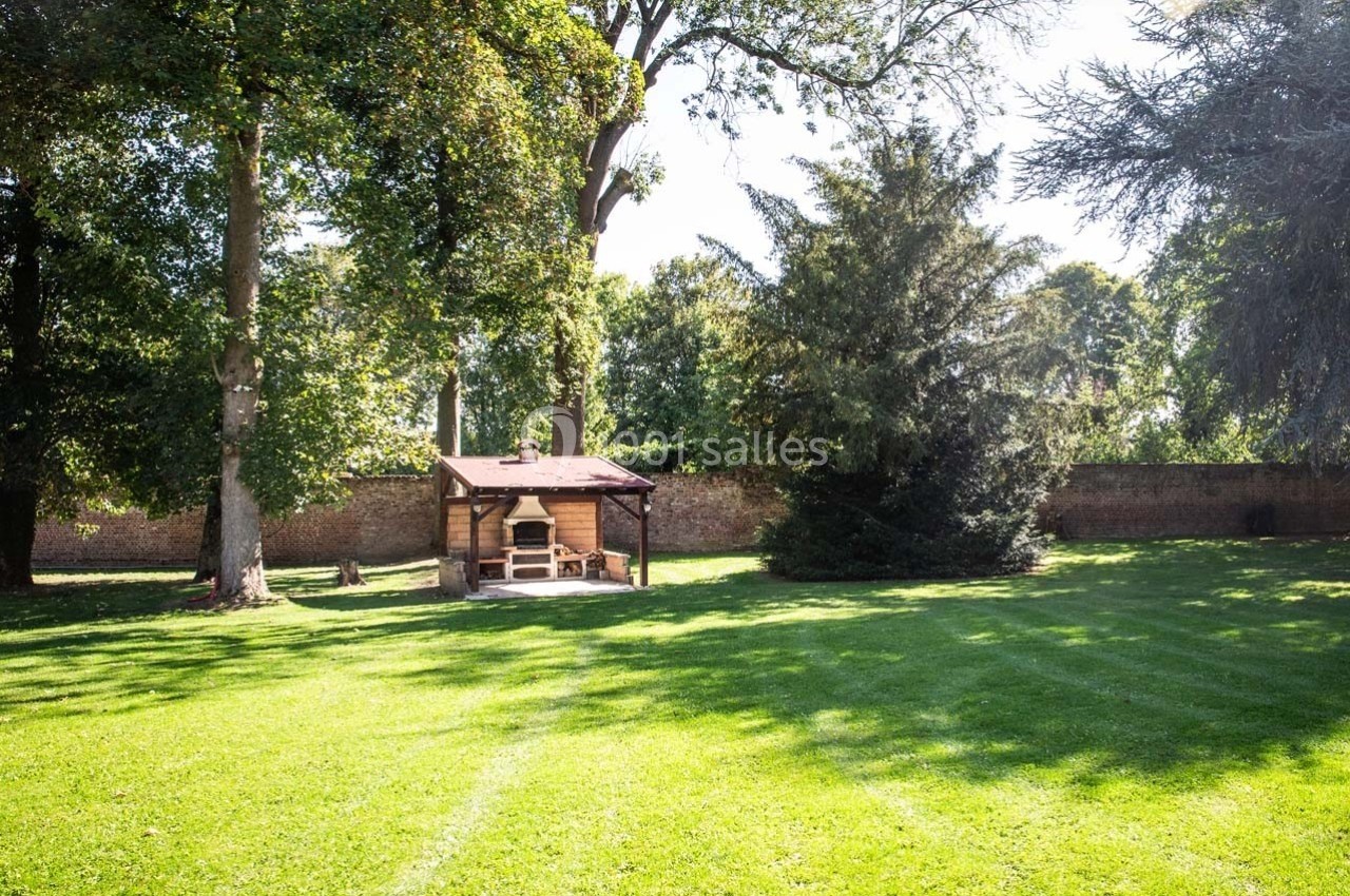 Pelouse verdoyante avec un abri en bois au centre, entourée d'arbres et d'un mur de briques en arrière-plan.