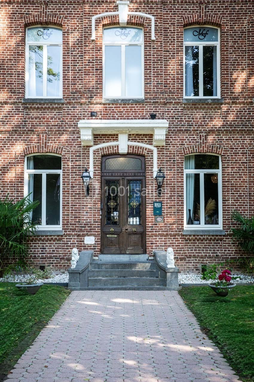 Façade en briques rouges d'une maison avec porte en bois, fenêtres blanches et allée pavée bordée de verdure.