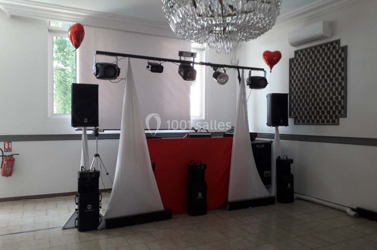 Installation de matériel de sonorisation et éclairage dans une salle avec un lustre et des ballons rouges en décoration.
