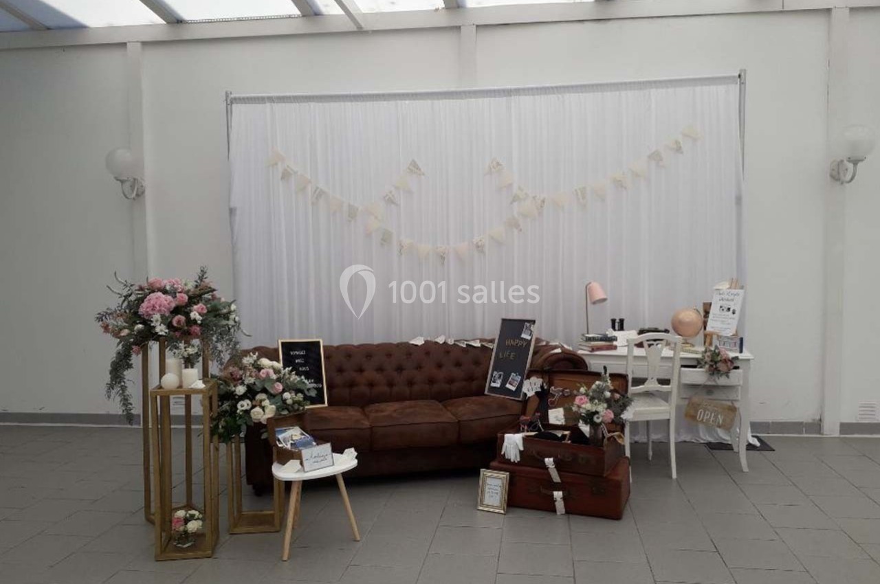 Décoration intérieure avec canapé en cuir, fleurs, valises et guirlandes dans un espace lumineux à fond blanc.