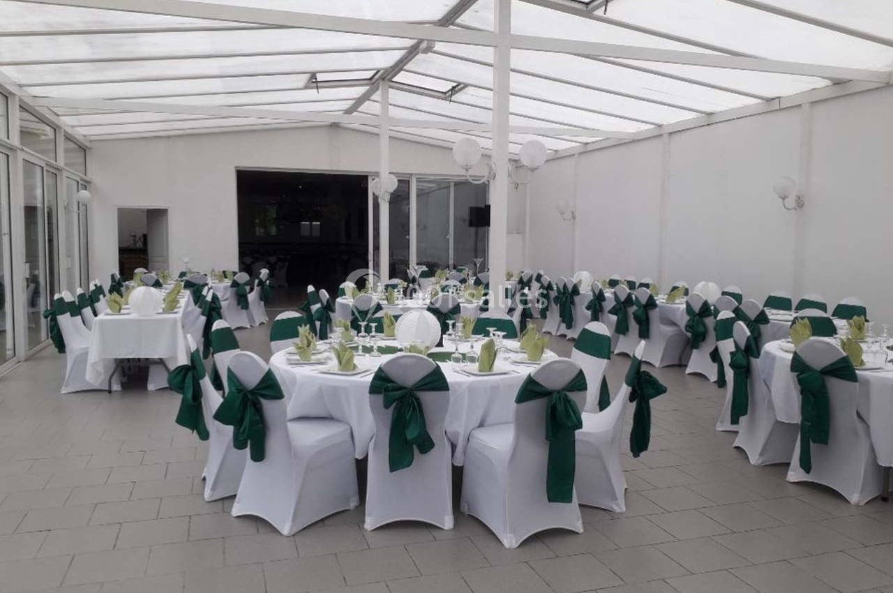 Salle de réception lumineuse avec tables rondes dressées et chaises blanches ornées de nœuds verts.