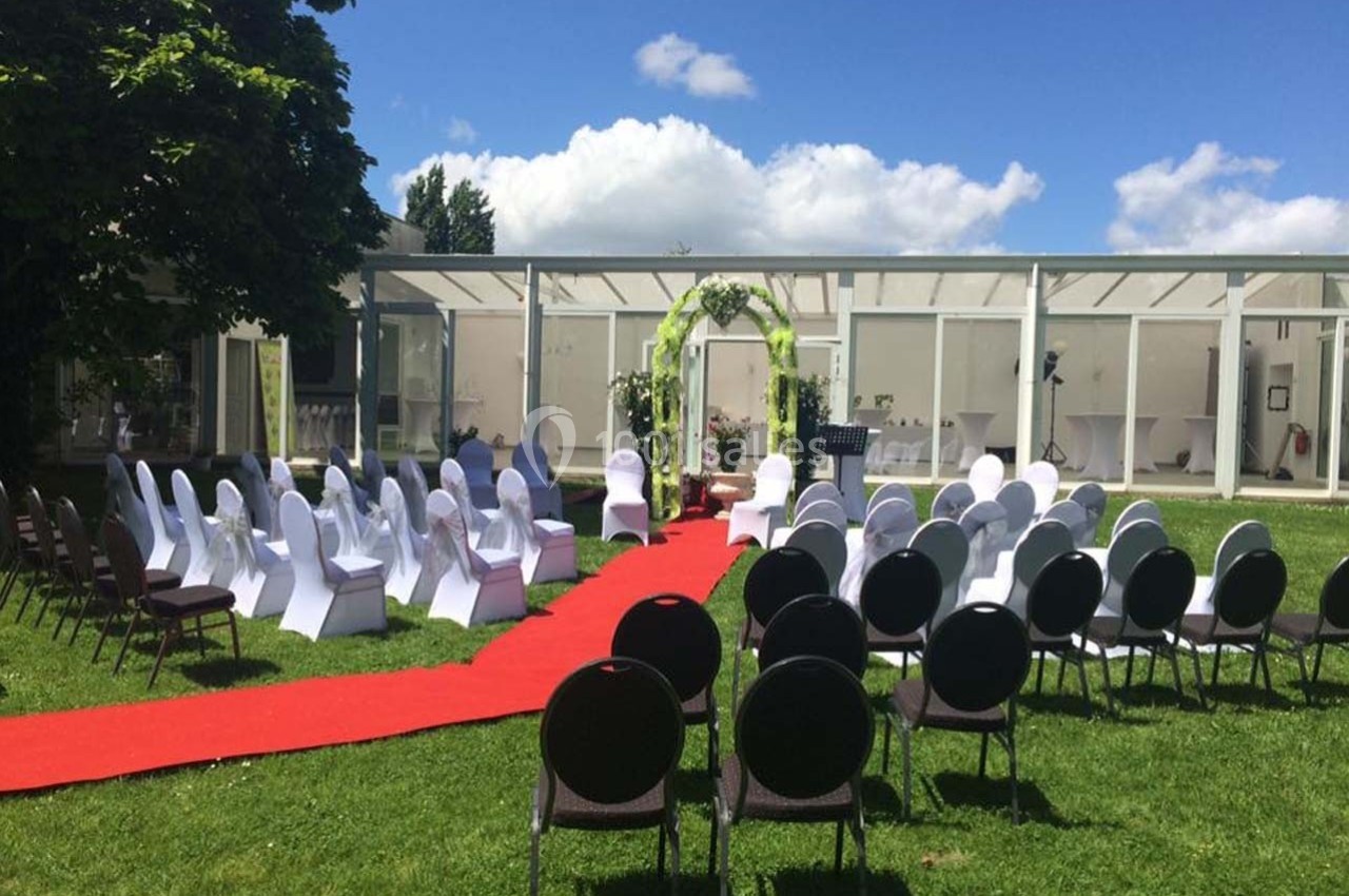 Chaises disposées en extérieur autour d'une allée rouge menant à une arche décorée pour une cérémonie.