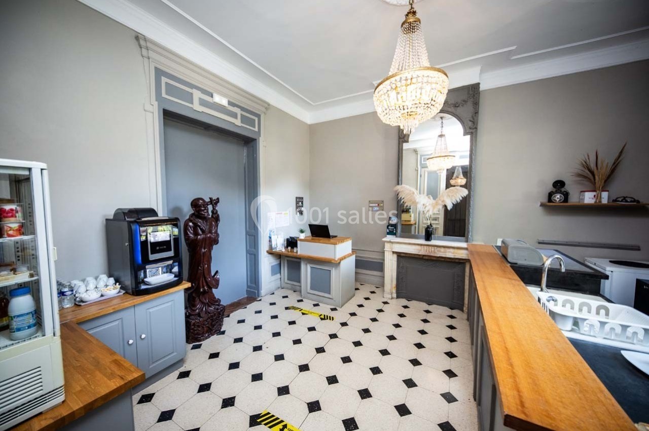 Salle d'accueil lumineuse avec comptoir en bois, sol à motifs, statue décorative et machine à café en libre-service.