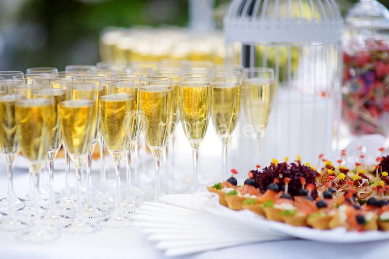 Verres de champagne alignés sur une table avec un plateau de bouchées apéritives en arrière-plan.