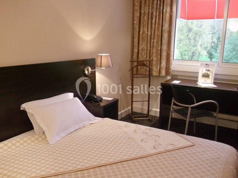 Chambre d'hôtel avec lit simple, bureau, chaise, lampe de chevet et fenêtre donnant sur un paysage verdoyant.