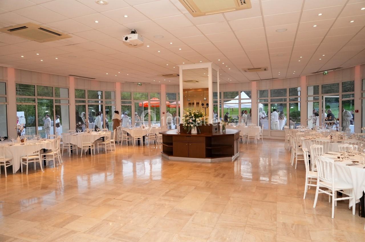 Salle de réception lumineuse avec tables dressées, grandes baies vitrées et vue sur un espace extérieur verdoyant.