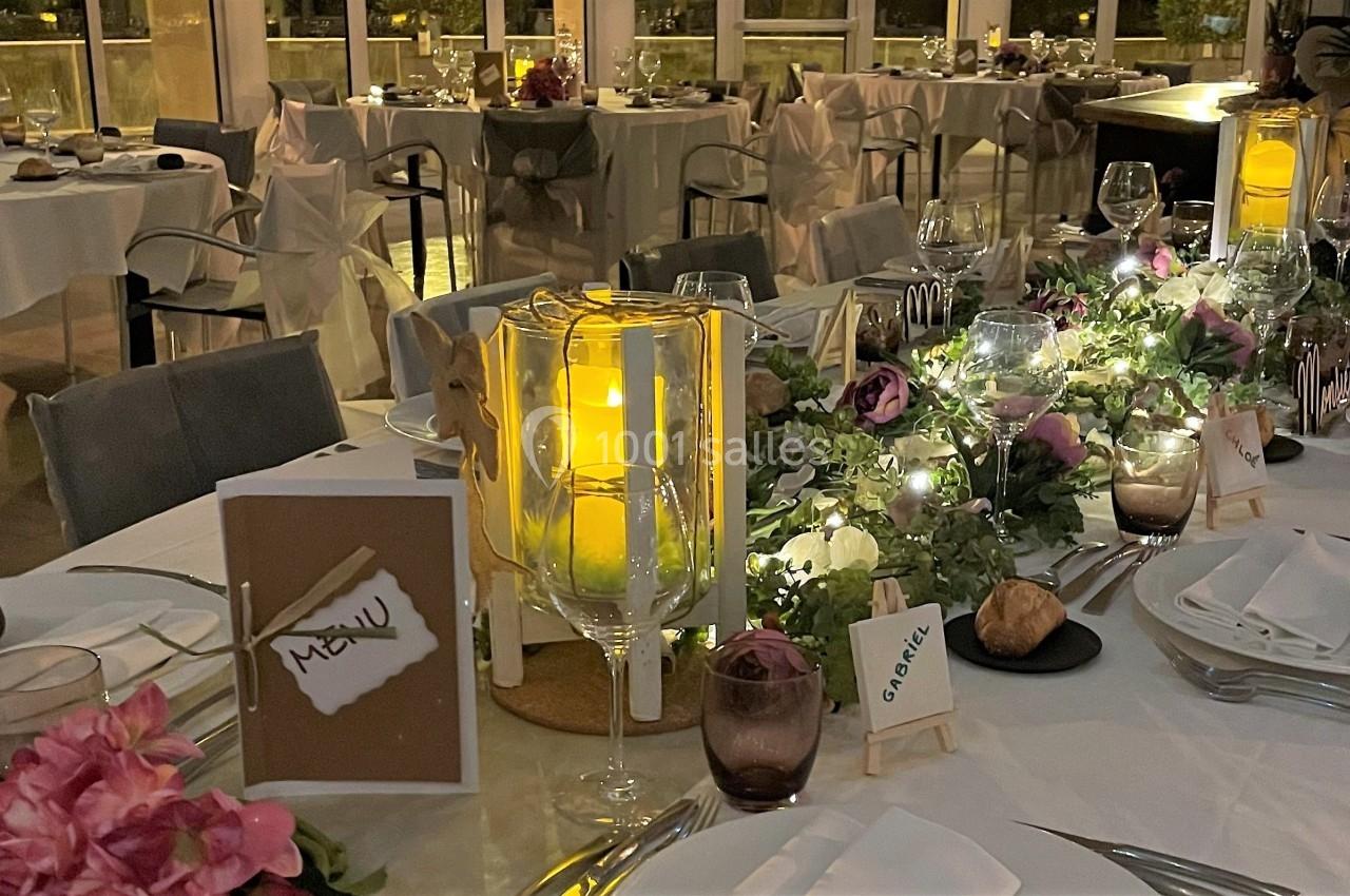 Table décorée pour un dîner élégant avec bougies, fleurs, menus et vaisselle, dans une salle éclairée en soirée.