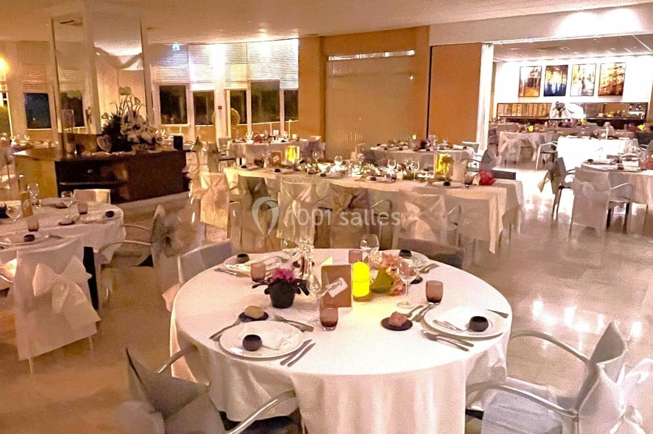 Salle de restaurant élégamment décorée, tables dressées avec nappes blanches et lumières tamisées.
