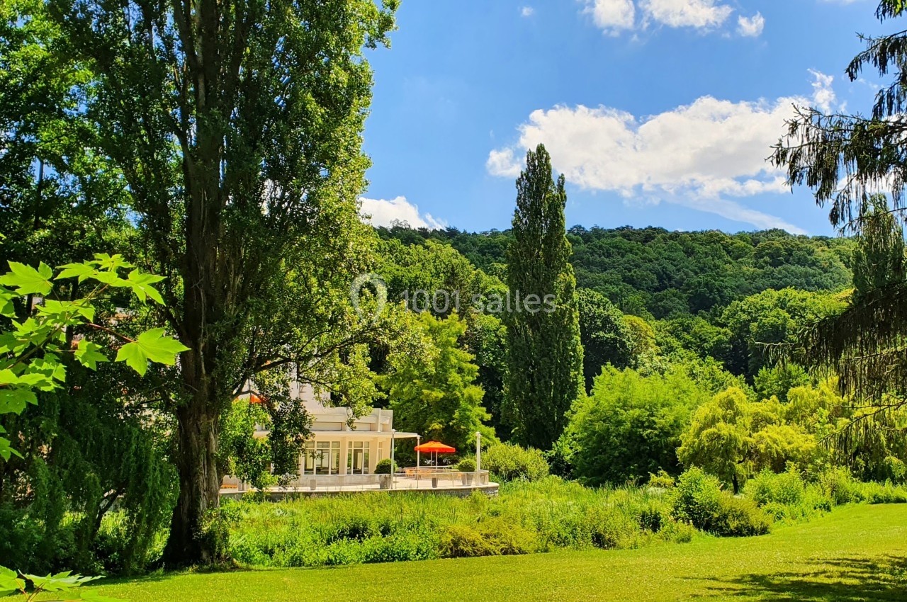 Parc verdoyant avec pelouse, arbres et bâtiment blanc en arrière-plan sous un ciel bleu.