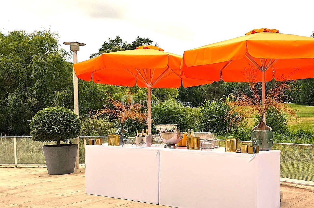 Table dressée en extérieur avec des parasols orange, entourée de verdure et d'un paysage arboré.