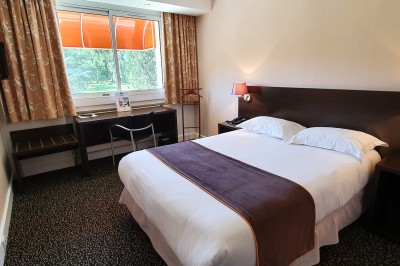 Chambre d'hôtel lumineuse avec un lit double, un bureau près d'une fenêtre et des murs partiellement violets.