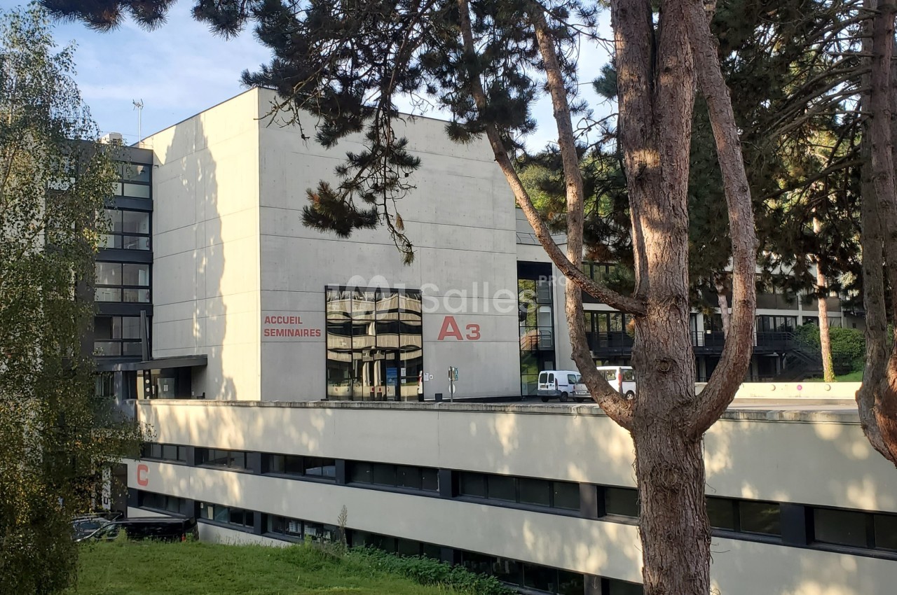 Bâtiment moderne entouré d'arbres, avec des fenêtres vitrées et des panneaux indiquant ’A3’ et ’Accueil’.
