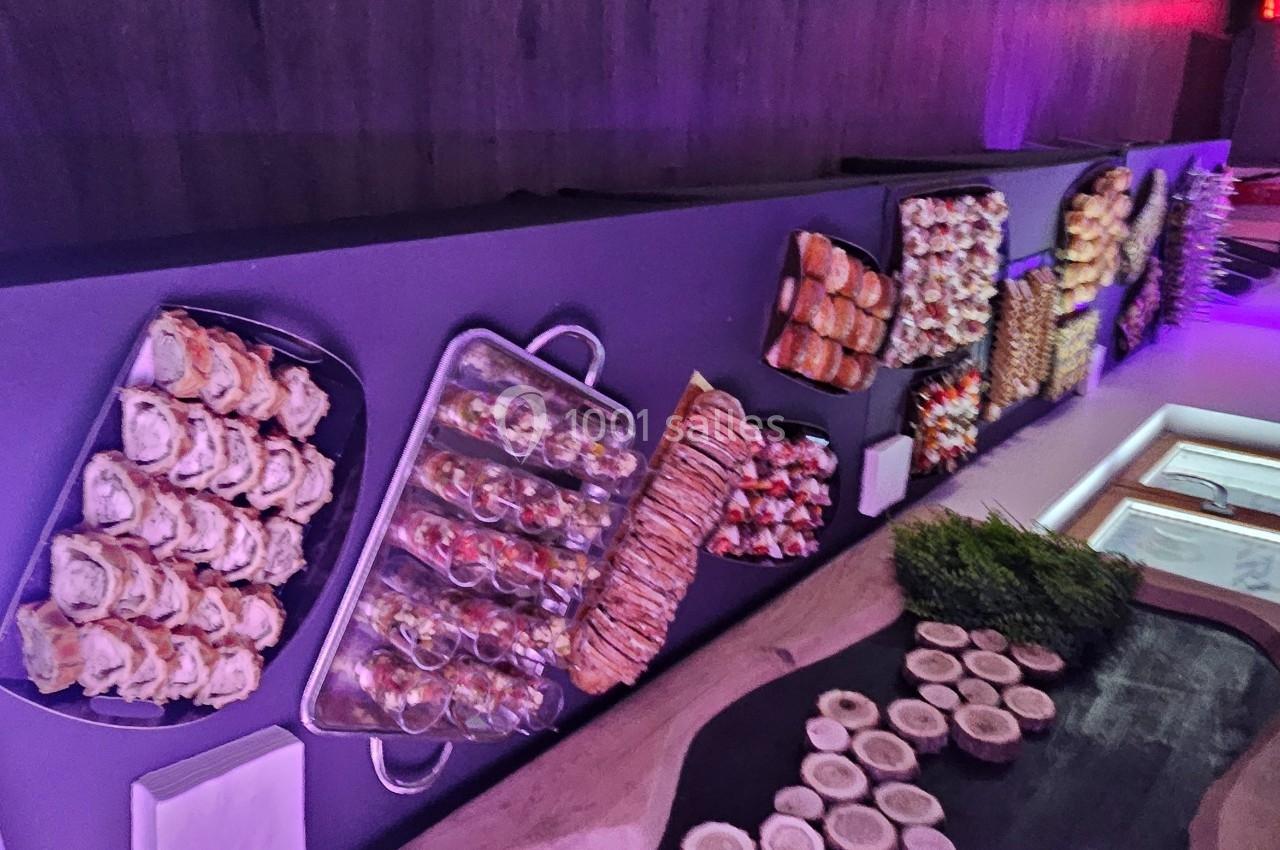 Buffet de plats variés disposés sur une table, éclairé par une lumière violette dans une salle moderne.