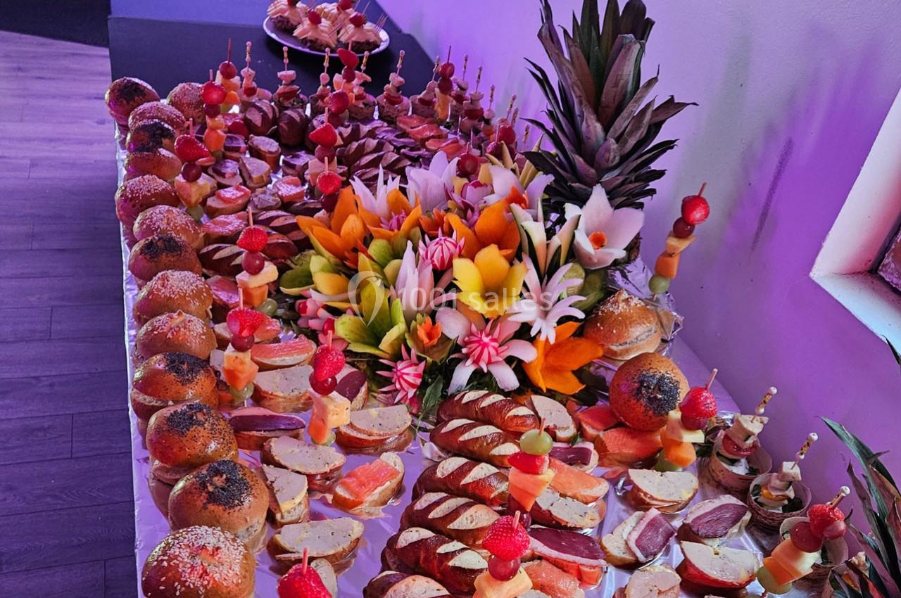 Plateau de buffet avec pains, fruits sculptés, brochettes de fruits et assortiments de charcuteries et fromages.