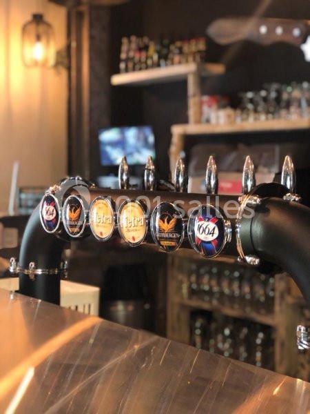 Tireuse à bière avec plusieurs robinets affichant des logos de marques, dans un bar à l'ambiance chaleureuse.